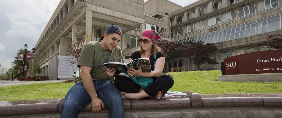 Students sitting outside of Faner looking at their BIO textbook